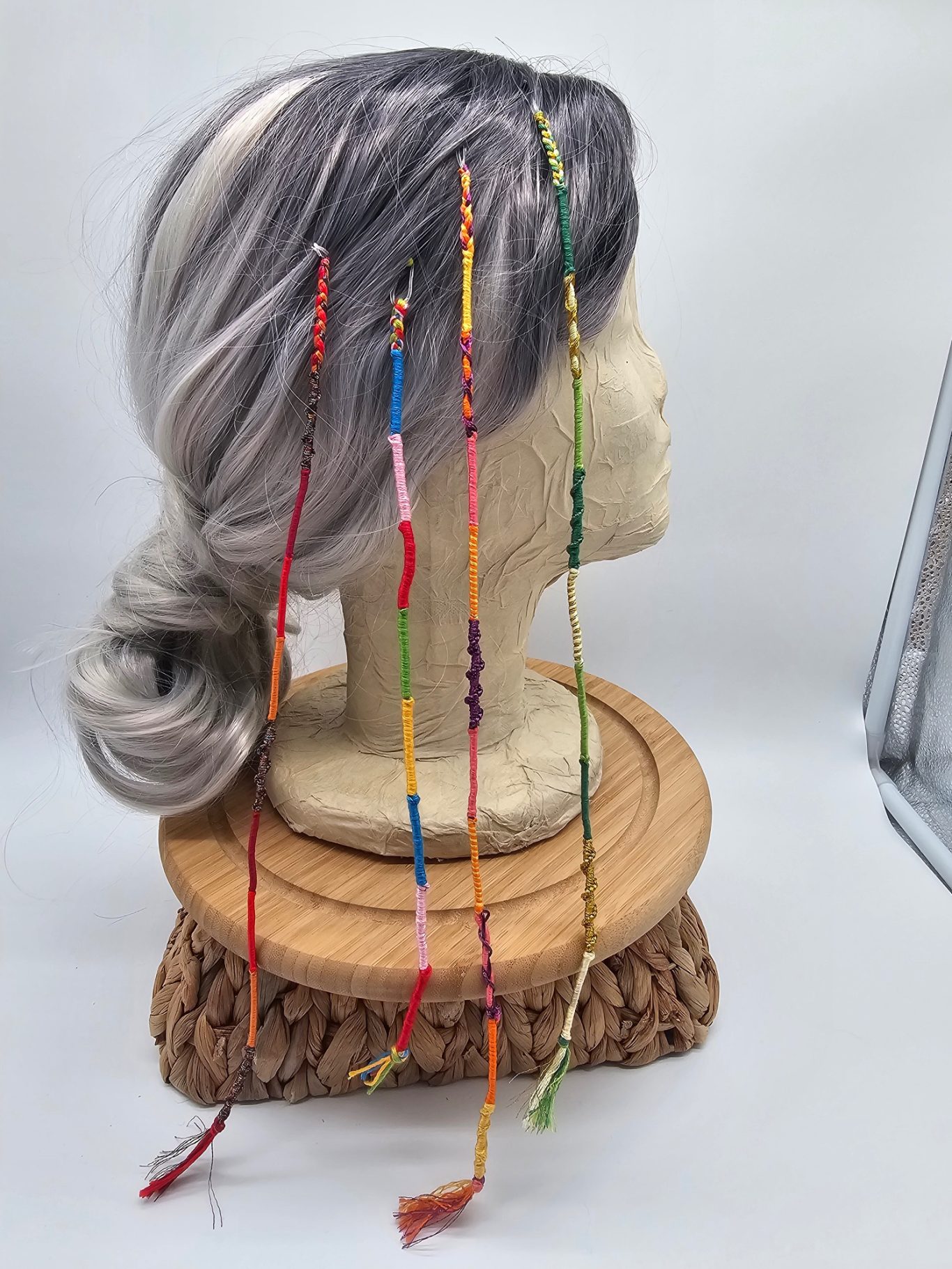 Haarsträhne Graue Perücke mit bunten, langen Haarsträhnen auf einem Holzständer.
