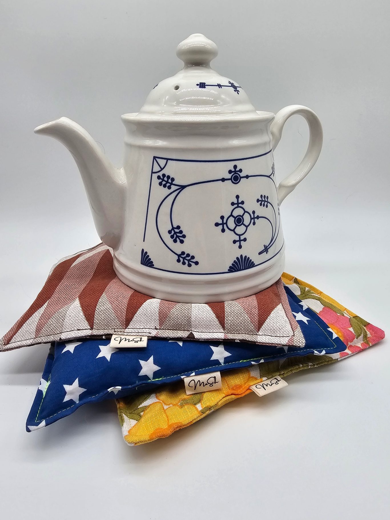 Upgecyceltes Teekannenwärmekissen Weiße Teekanne mit blauem Muster auf bunten Tekannenwärmekissen.