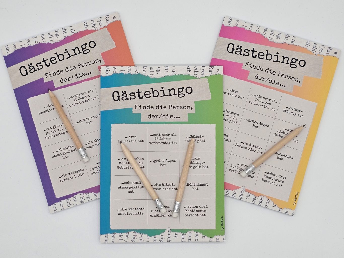 Gästebingo Drei bunte Bingo-Karten-Blöcke mit Bleistiften auf einem Tisch.