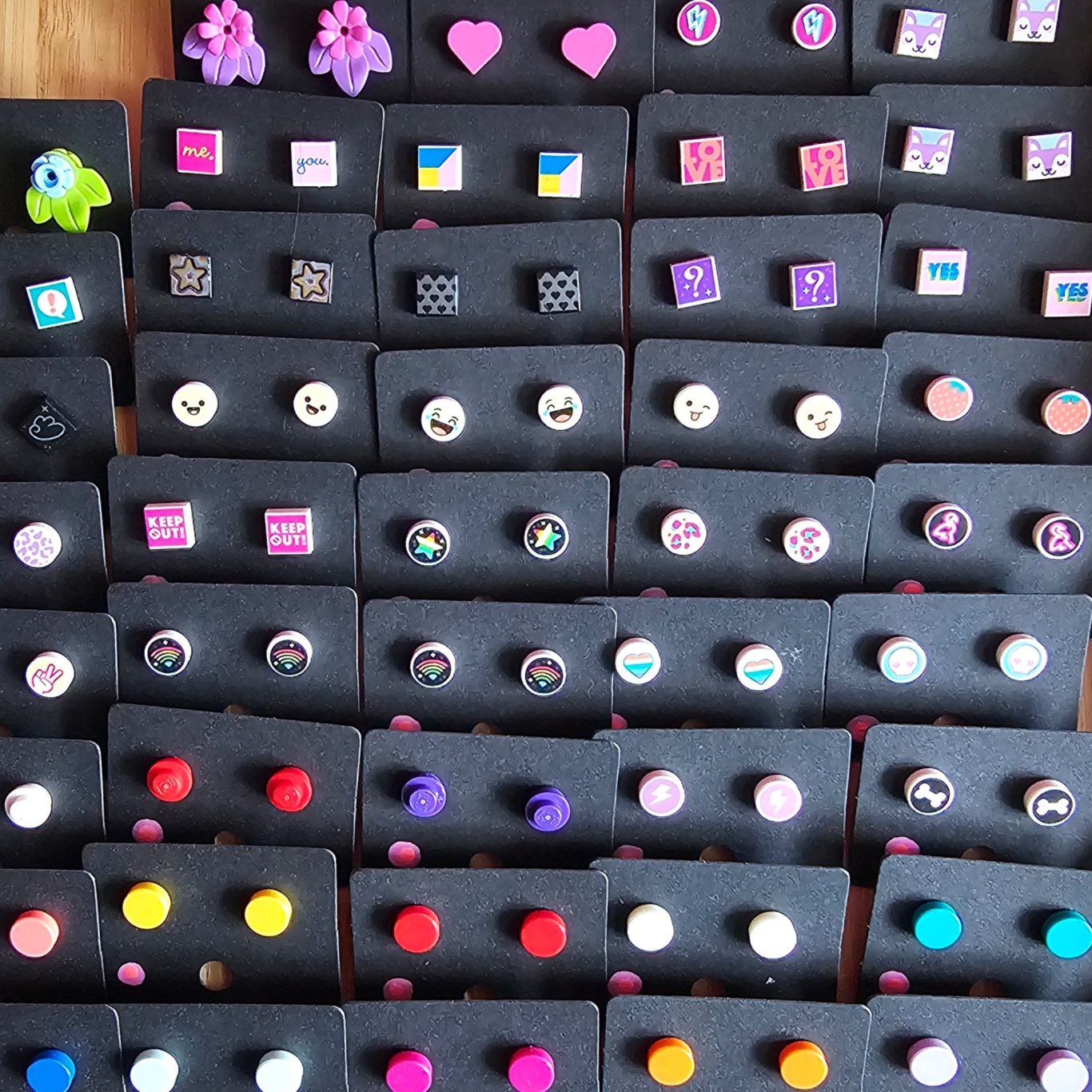 Upgecycelte Ohrstecker (Edelstahl) Verschiedene bunte Ohrringe mit Legosteinen in mehreren Reihen auf schwarzem Grund.