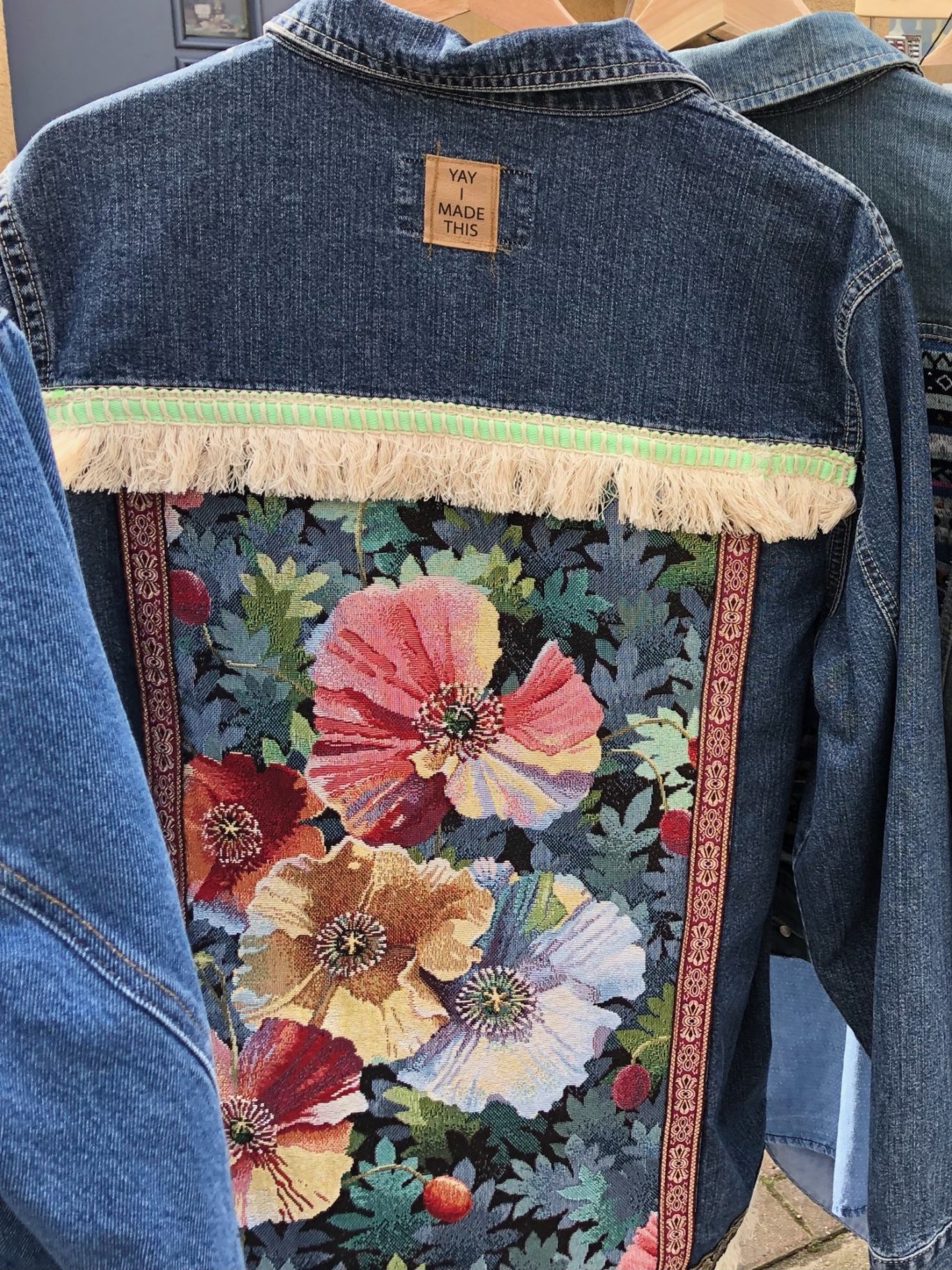 Upgecycelte Blumenjeansjacke Jeansjacke mit buntem Blumenmuster und Fransen an der Rückseite.