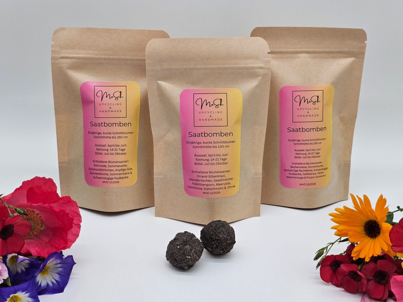 Saatgutbomben Drei Verpackungen mit Saatgutbomben mit zwei Saatgutkugeln und dekorativen Blumen im Vordergrund.