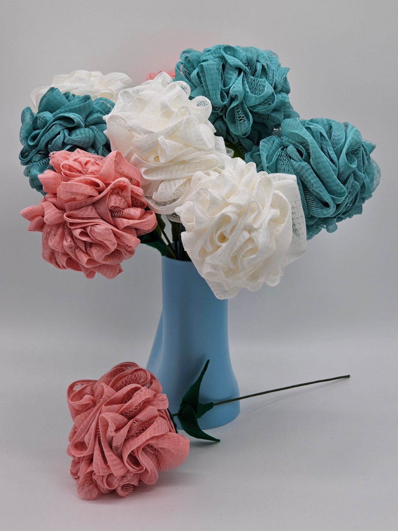 Upgecycelte Schwammblumen Buntes, kunstvolles Blumenarrangement aus Badeschwämmen in einer blauen Vase.