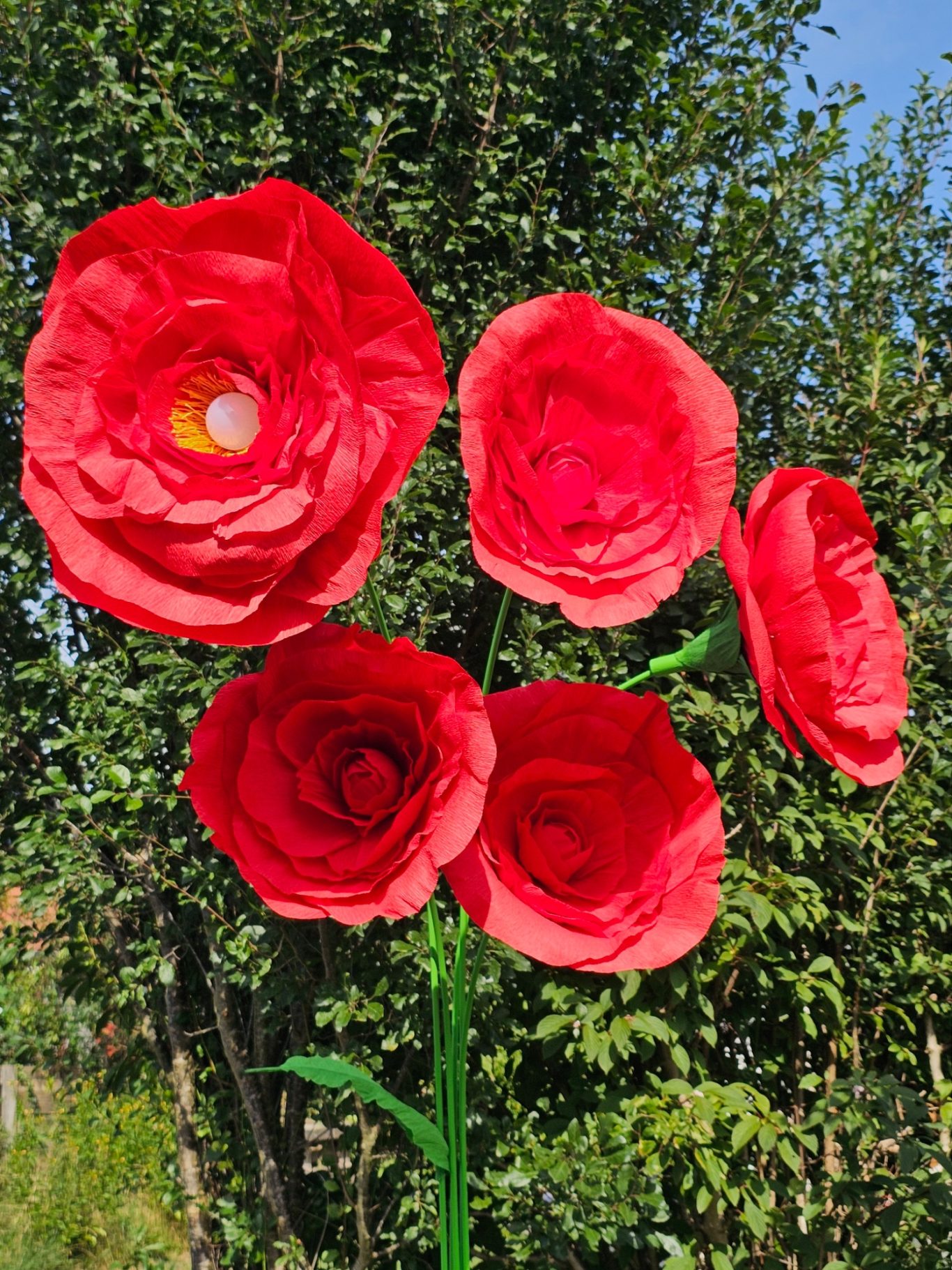 Upgecycelte Blumenlampe Fünf große rote Rosenblüten vor grünem Hintergrund.