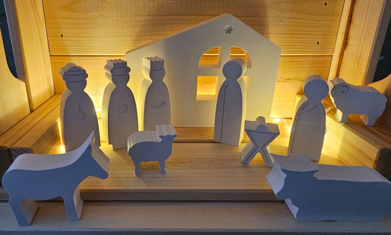 Gegossene Krippe Aus Resin gegossene Figuren einer Krippe mit Tieren und Personen, sanft beleuchtet im Hintergrund.