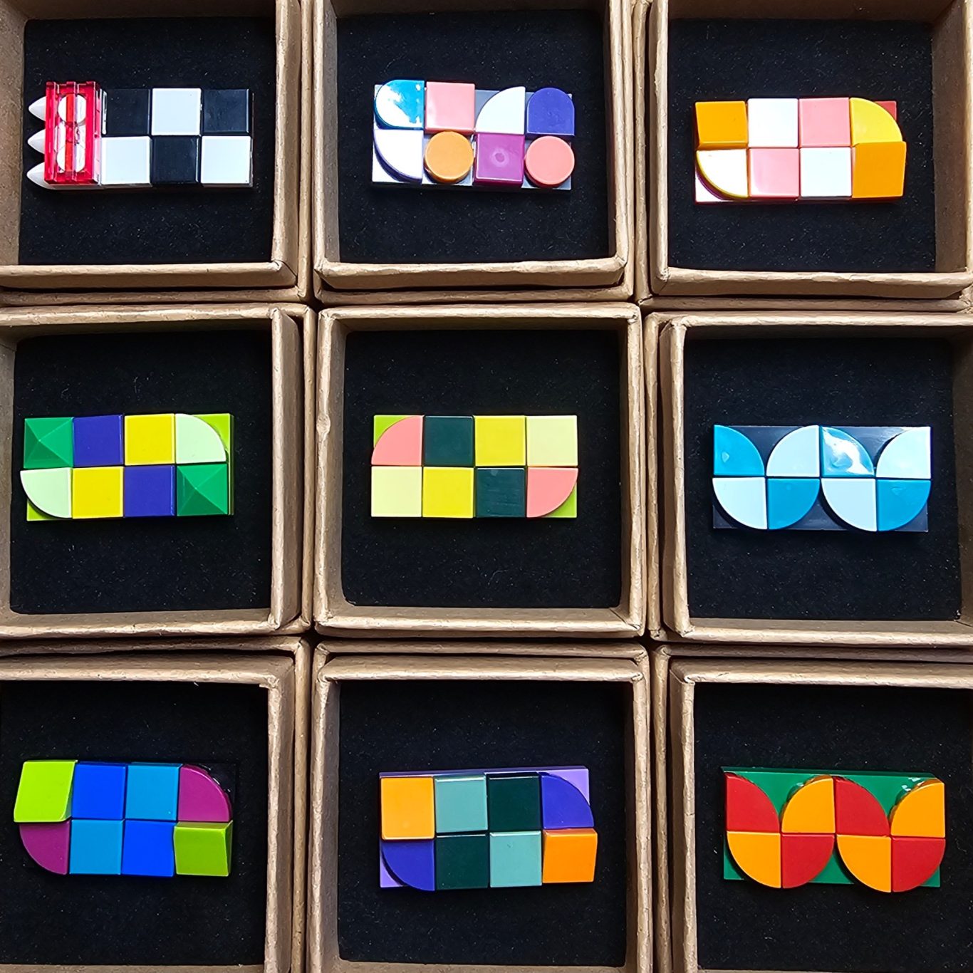 Upgecycelte große Brosche Bunte geometrische Formen aus Legosteinen als Brosche in quadratischen Kästchen auf schwarzem Hintergrund.