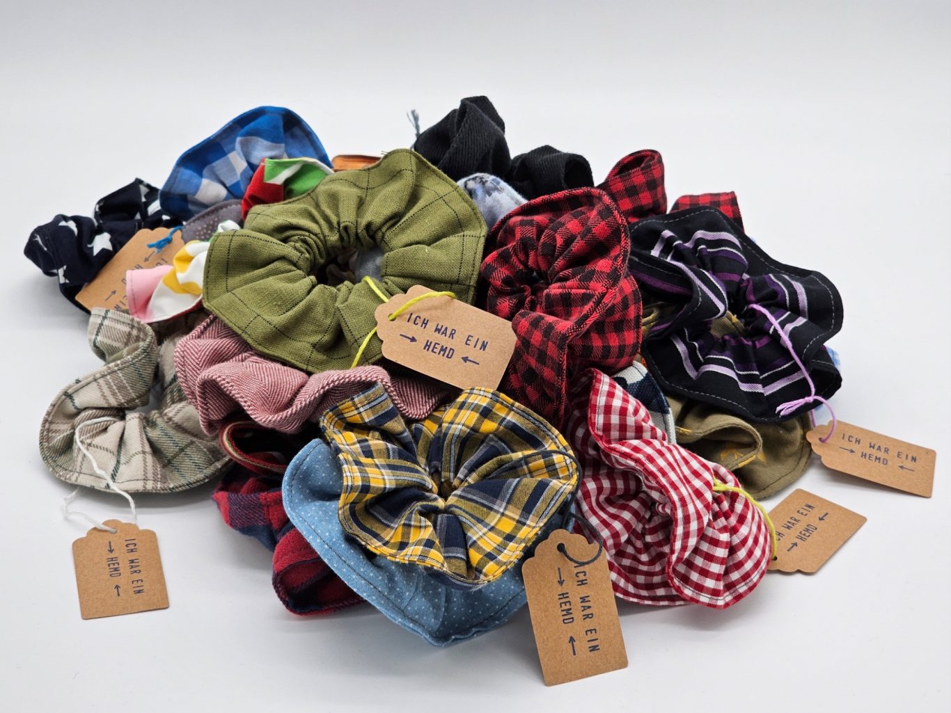 Upgecyceltes Scrunchie (Haargummi) Bunte Scrunchies (Haargummis) in verschiedenen Mustern und Farben, mit kleinen Etiketten.