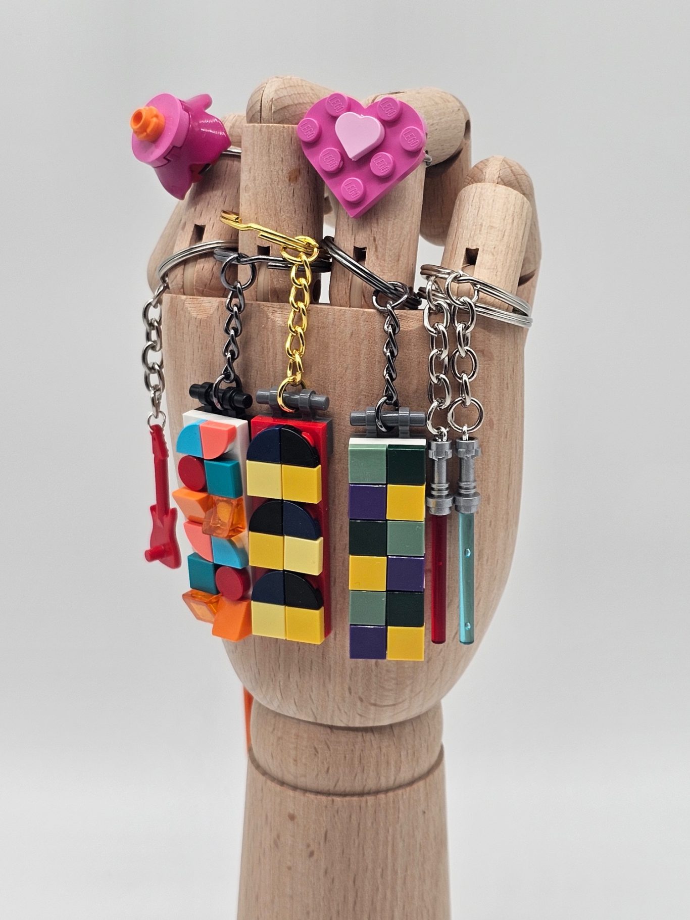 Upgecycelte Schlüsselanhänger & Ringe aus Legosteinen Bunte Schlüsselanhänger und Ringe auf einem Handmodell aus Holz.